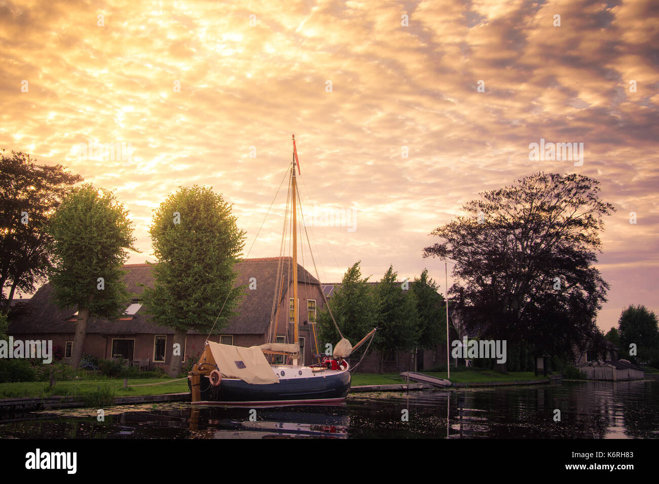 Una barca a vela olandese tradizionale barca ancorata in un canale esterno di una casa con la golden cielo nuvoloso, Holland, Paesi Bassi. Foto Stock
