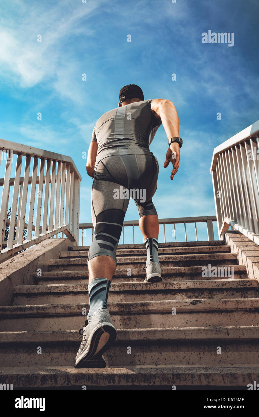 Giovane sportivo muscolare in esecuzione su per le scale fino al ponte. vista posteriore. Foto Stock