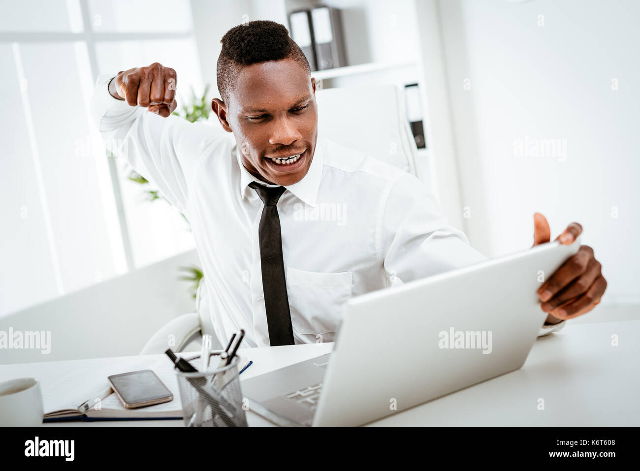 Furioso imprenditore africano getta un punzone nel portatile in ufficio. Foto Stock