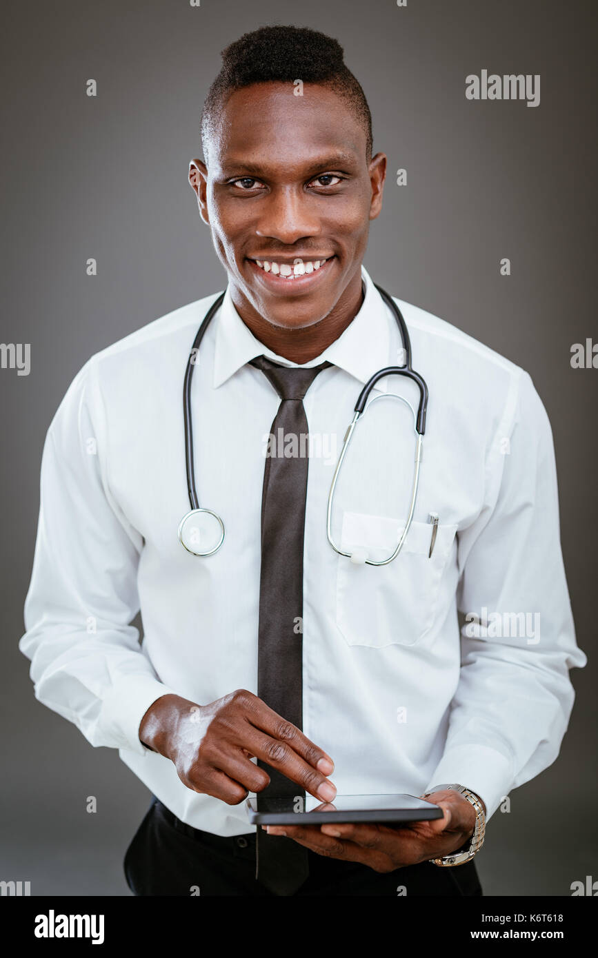 Sorridente africana medico con stetoscopio e permanente con tavoletta digitale. guardando la fotocamera. Foto Stock