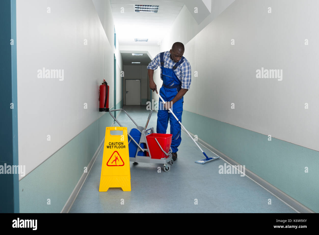 Ritratto di giovane africano bidello maschio pulizia pavimento in corridoio Foto Stock
