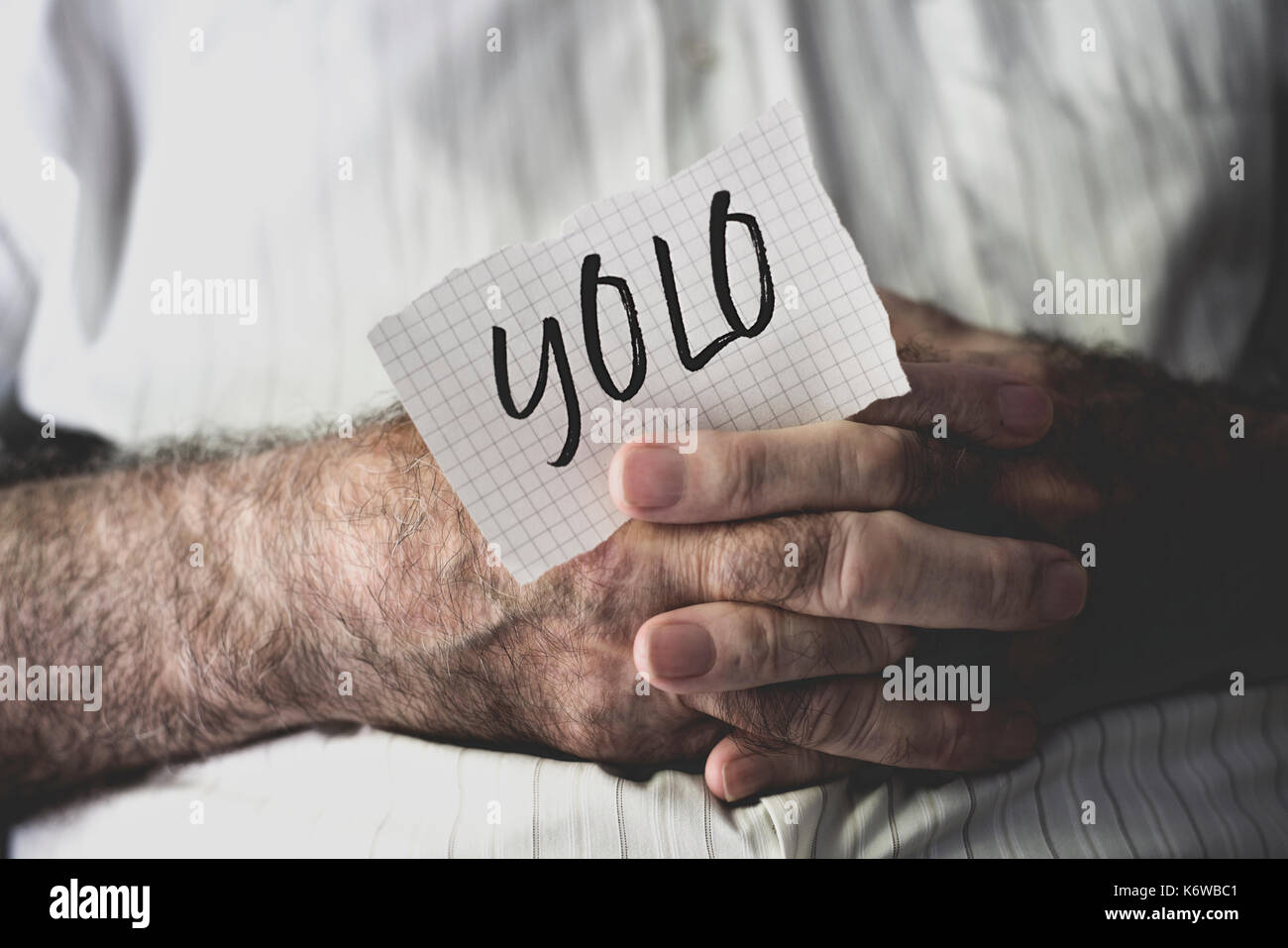 Primo piano di un vecchio uomo caucasico con una nota nelle sue mani con la parola yolo, per si vive una volta sola, scritto in esso Foto Stock