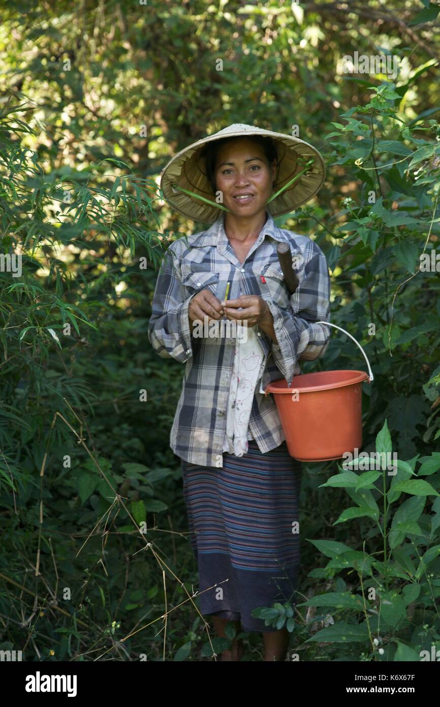 Laos, Champassak, donna che indossa un cappello concial di paglia con un secchio sotto il braccio nel sottobosco Foto Stock