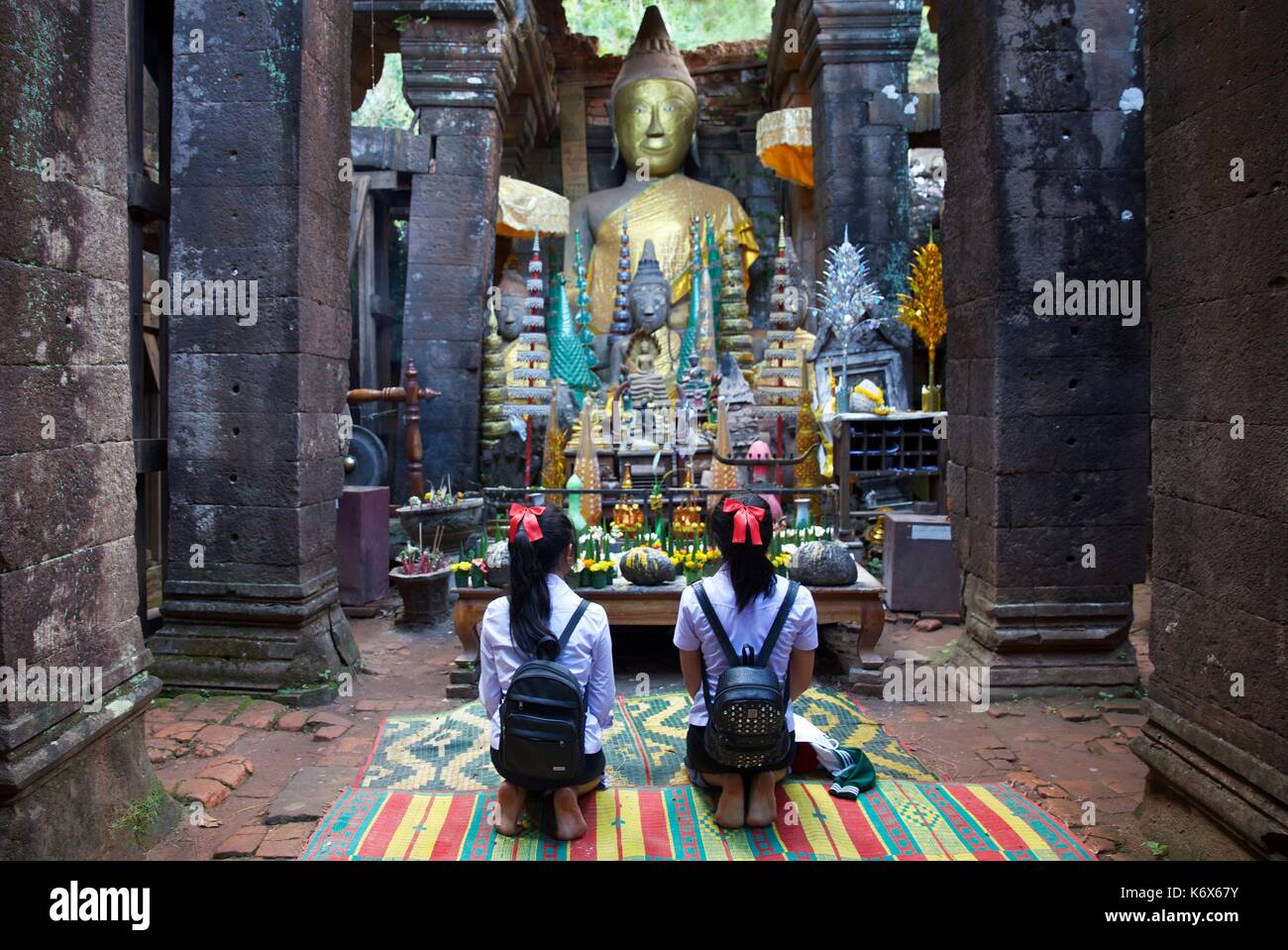 Laos, Champassak, Vat Phou, classificato come patrimonio mondiale dall UNESCO, due schoolgilrs prosternerà se stessi di fronte ad una statua di Buddha nel tempio bouddist di Vat Phou Foto Stock