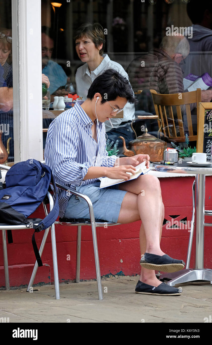 Giovane maschio persona seduta al di fuori cafe libro, Cambridge, Inghilterra Foto Stock