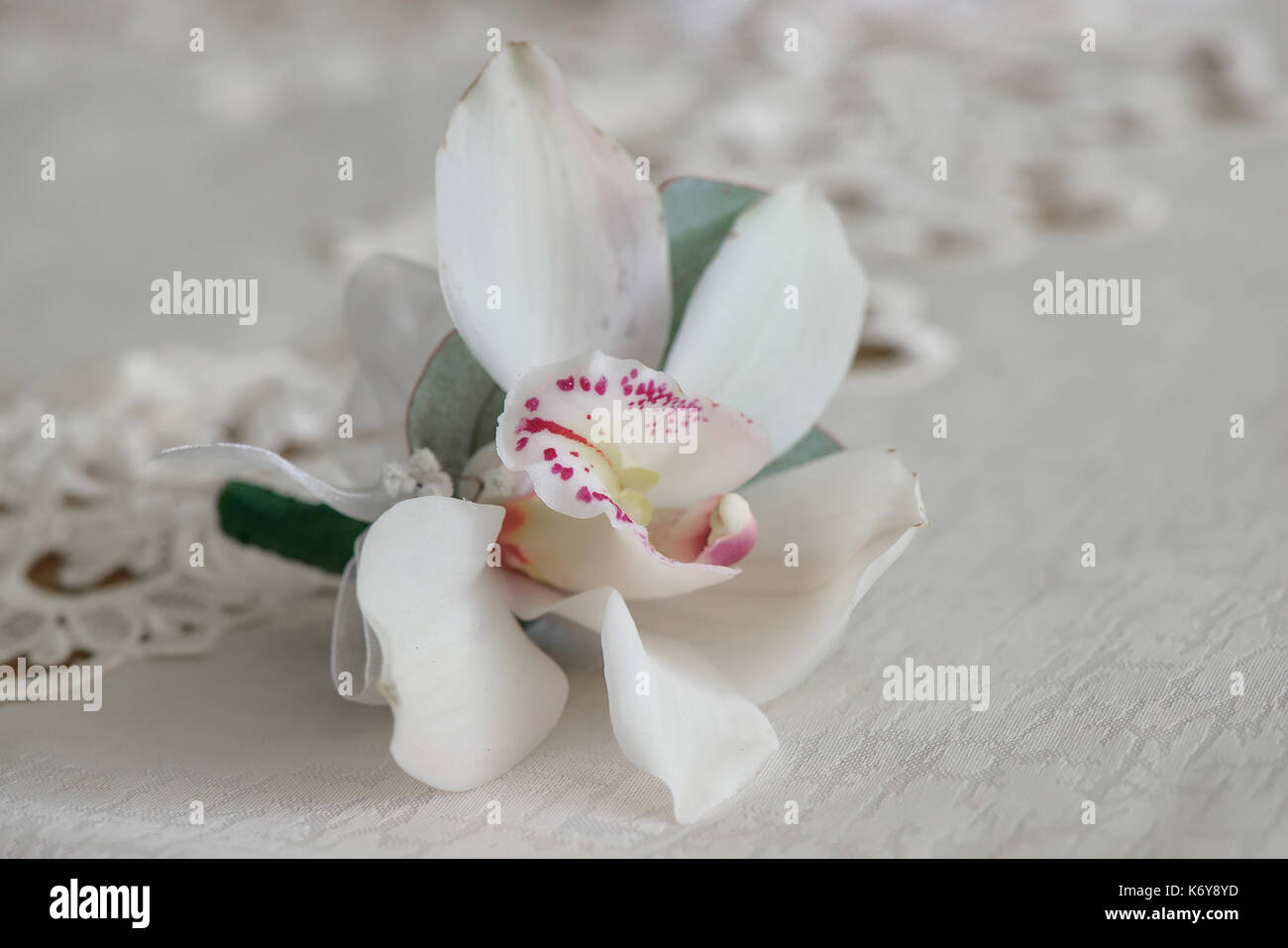 White Orchid boutonniere piccolo bouquet per asola utilizzato per lo sposo e gli invitati a nozze posizionato su un panno bianco, in presenza di luce naturale. Foto Stock