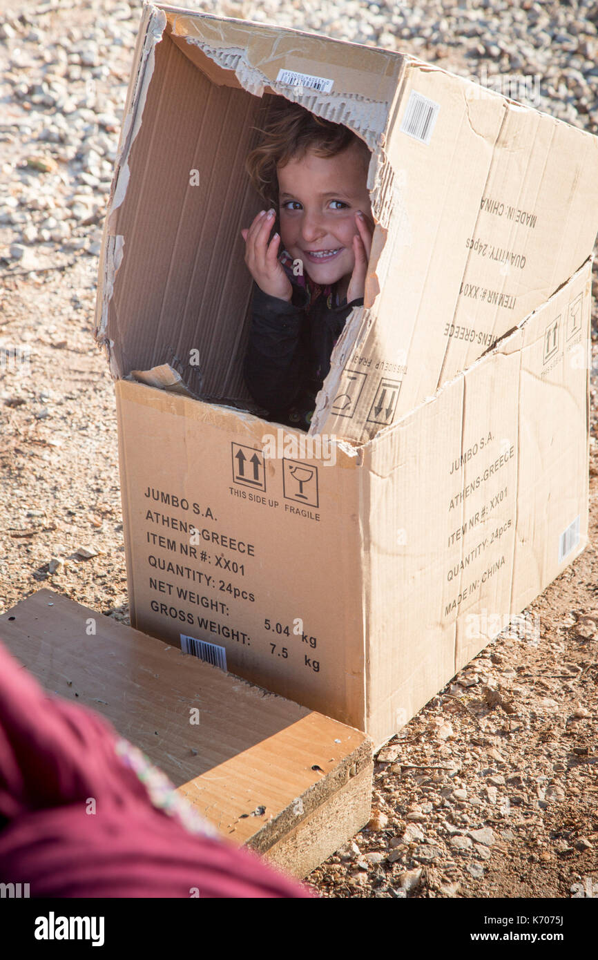 Un bambino gioca felicemente, nascondendosi in una scatola di cartone sul fosco pietraie di ritsona Refugee Camp in Grecia. Foto Stock