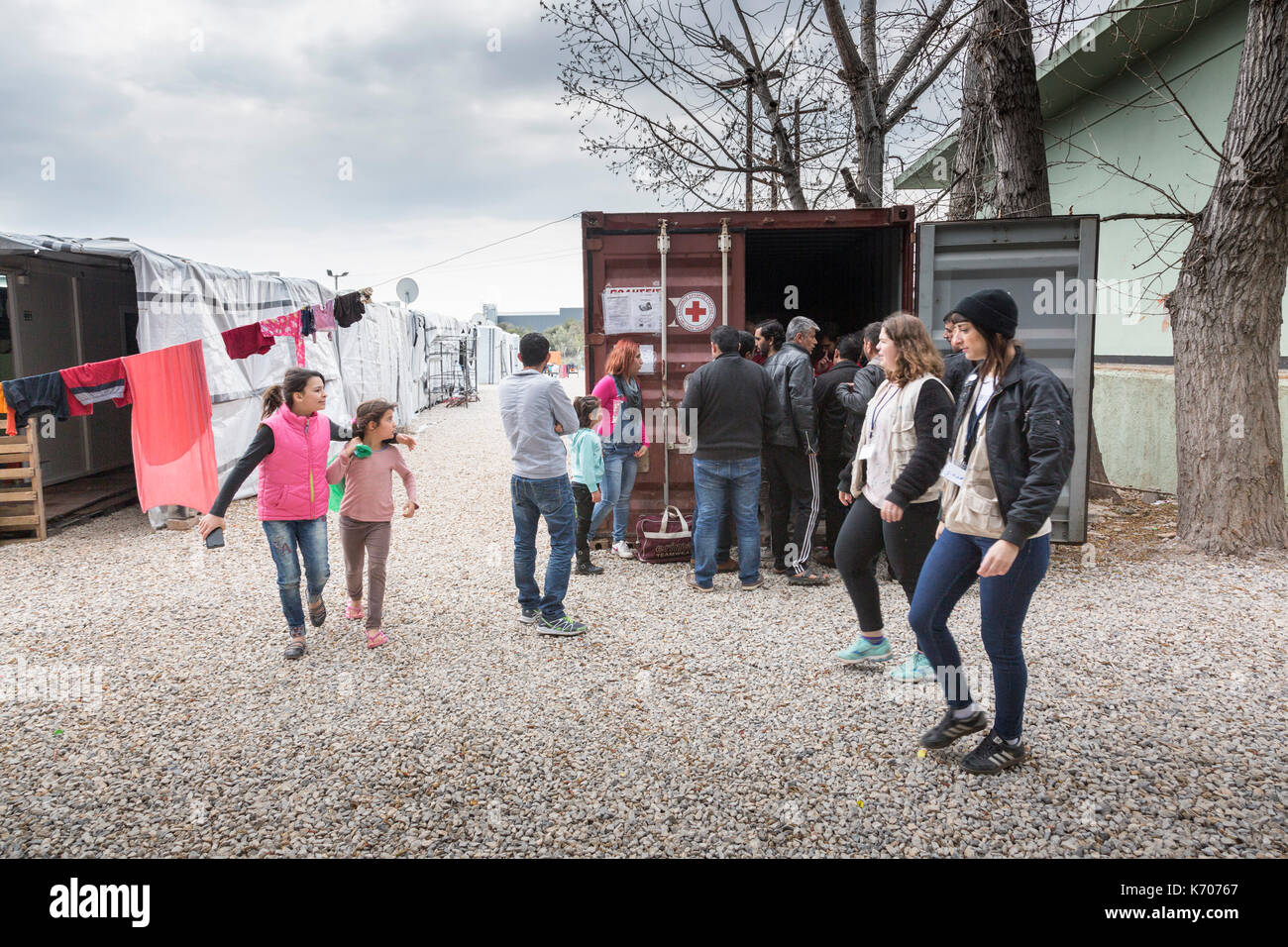 Al ritsona Refugee Camp in Grecia, gli uomini si riuniscono da un contenitore di spedizione, utilizzato come ufficio e centro di distribuzione dalla Croce Rossa Greca. Foto Stock