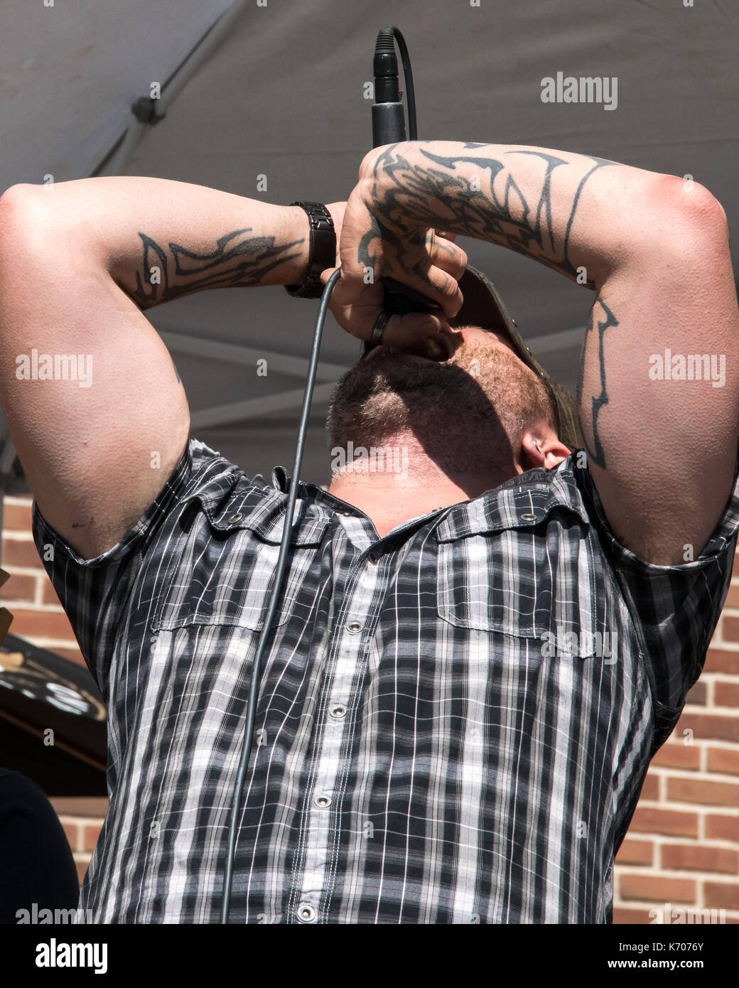 Un forte caucasian indossando un bianco e nero plaid shirt cantante rock cinghie fuori una canzone e un locale festival di musica. Foto Stock