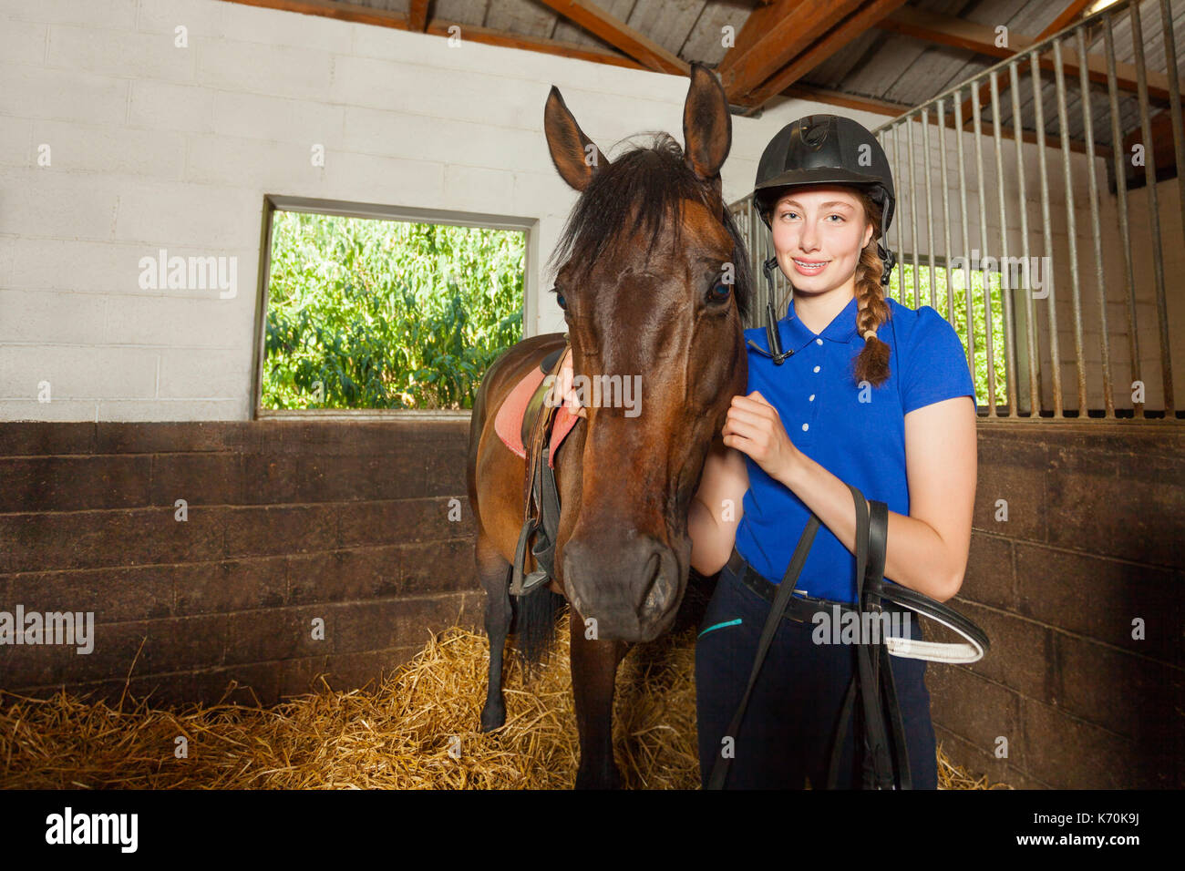 Bellissima femmina permanente jockey dentro la stalla e abbracciando il suo cavallo di baia Foto Stock