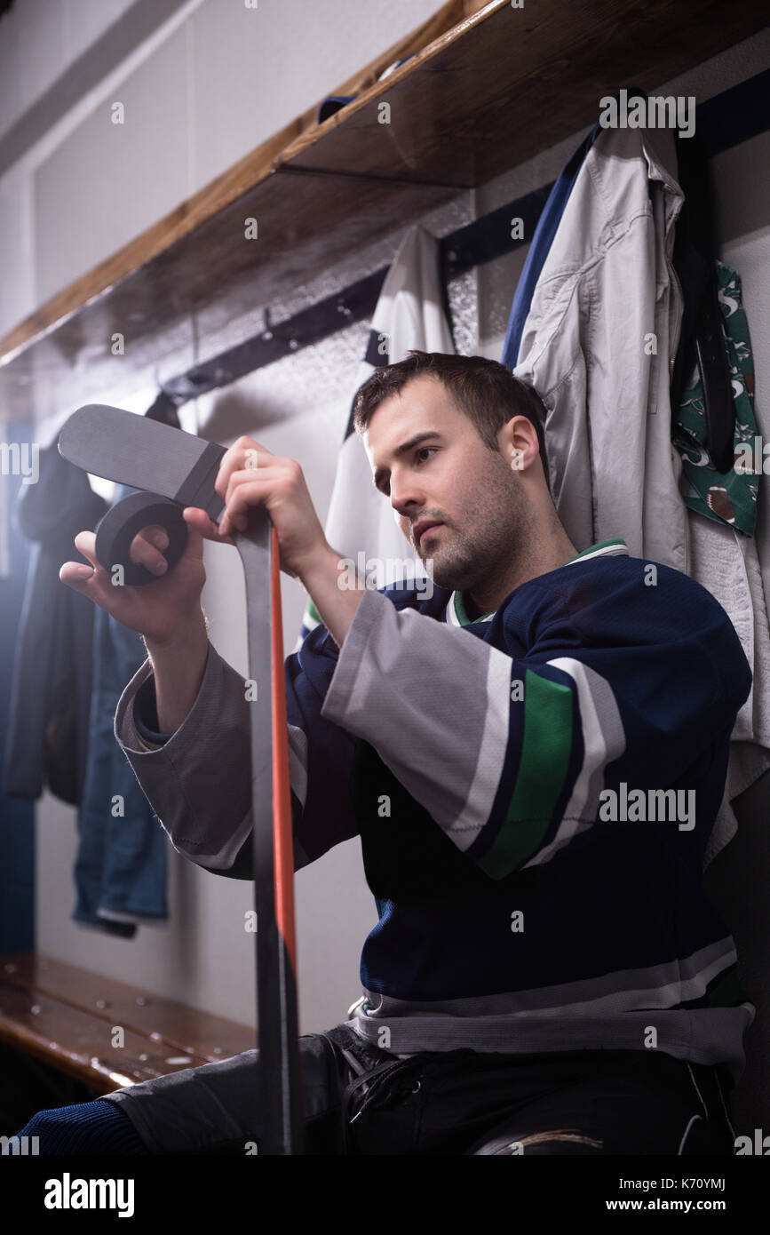 Lettore maschio taping ice hockey stick mentre è seduto in spogliatoio Foto Stock