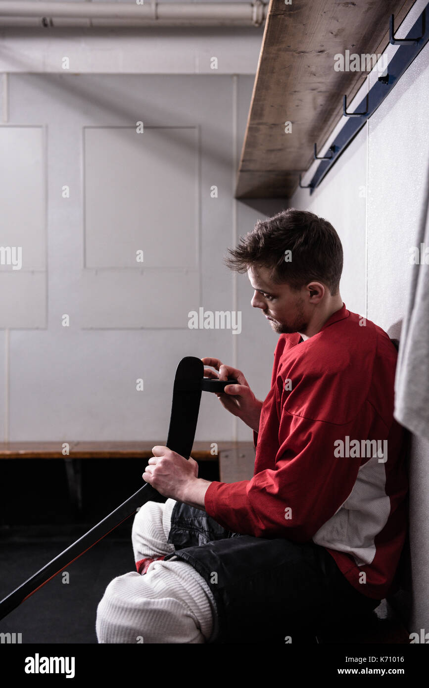 Vista laterale del lettore maschio taping ice hockey stick in spogliatoio Foto Stock