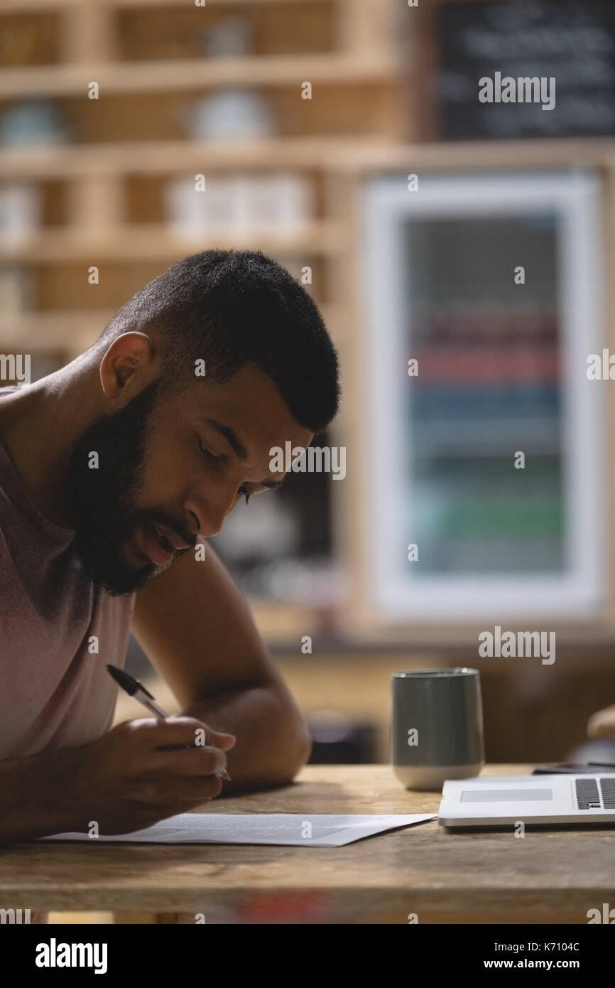 Chiusura del giovane di scrittura mentre è seduto con il computer portatile in cafe Foto Stock