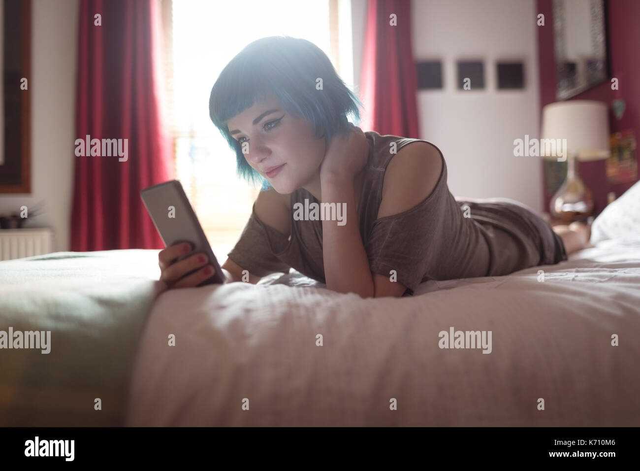 Giovane donna usando il telefono mentre vi rilassate sul letto di casa Foto Stock