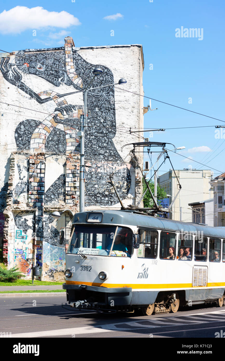 Pendolari su un vecchio tram nella periferia di Bucarest con artwork sul lato di un edificio che si trova dietro. Foto Stock
