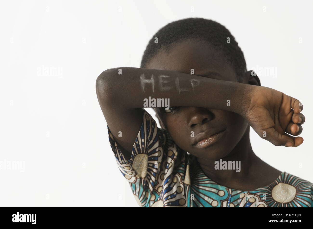 Little Boy africana chiede aiuto coprendo il viso con il suo braccio, isolato su bianco Foto Stock