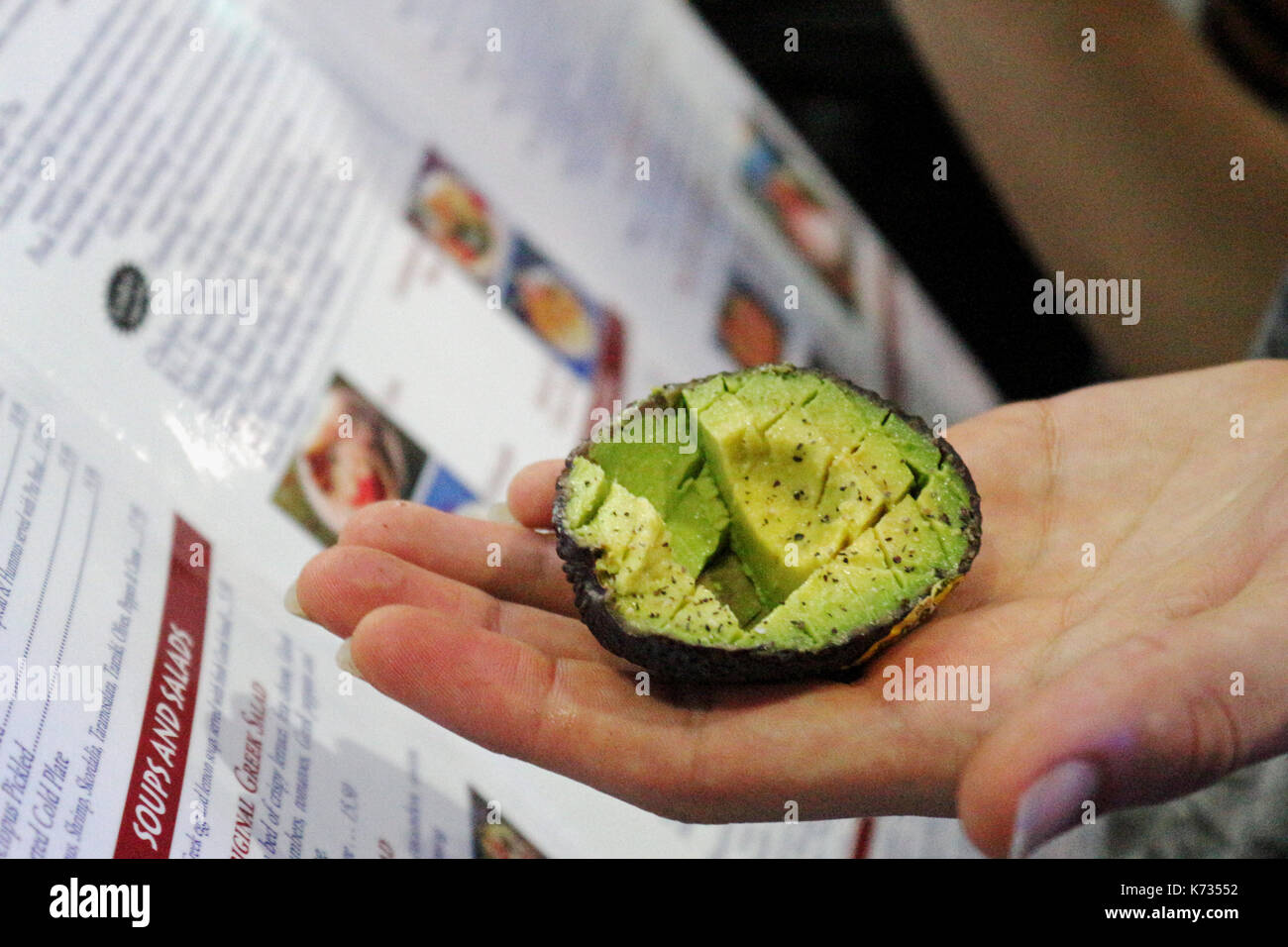 Un affettato avocado seduto su una mano pronta da mangiare con un menù del ristorante in background. Foto Stock