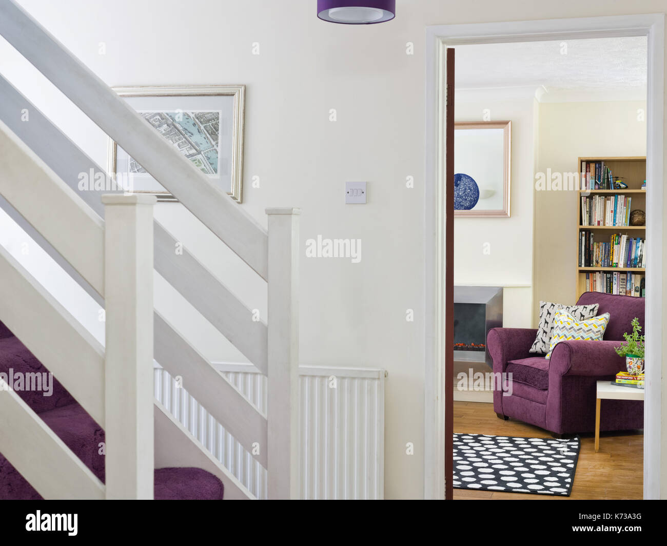 Le scale in una tipica casa del Regno Unito's hall di ingresso con una vista in una stanza di seduta che mostra una comoda poltrona di colore viola e altri mobili Foto Stock