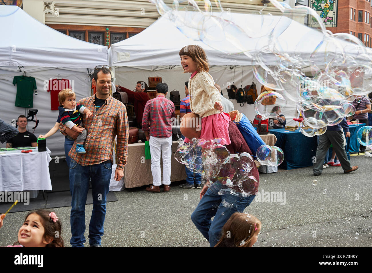 Bambini e adulti Genitori giocare con bolle aventi divertimento su una London street fair fayre UK Gran Bretagna Foto Stock