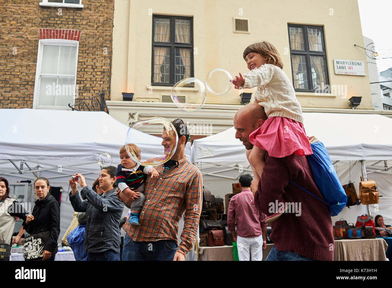 Bambini e adulti Genitori giocare con bolle aventi divertimento su una London street fair fayre UK Gran Bretagna Foto Stock