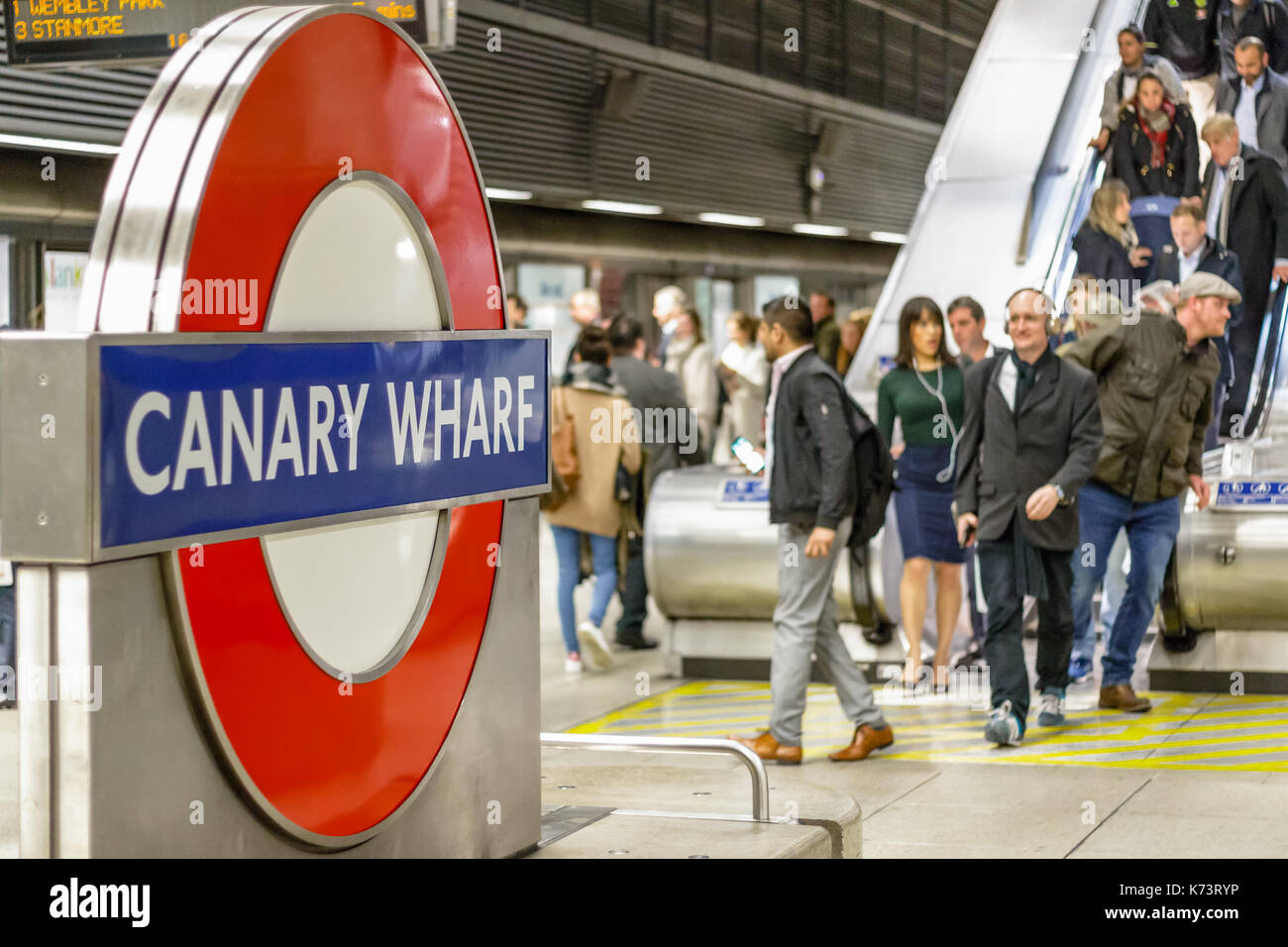 London, Regno Unito - 15 settembre 2017 - metropolitana di Canary Wharf segno con una folla di pendolari provenienti in giù su un Escalator in background Foto Stock