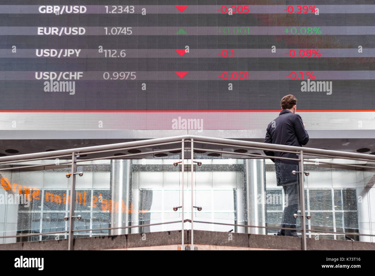 London, Regno Unito - 15 settembre 2017 - Mercato azionario i dati visualizzati su uno schermo esterno in canary wharf con un uomo in piedi di fronte ad essa Foto Stock