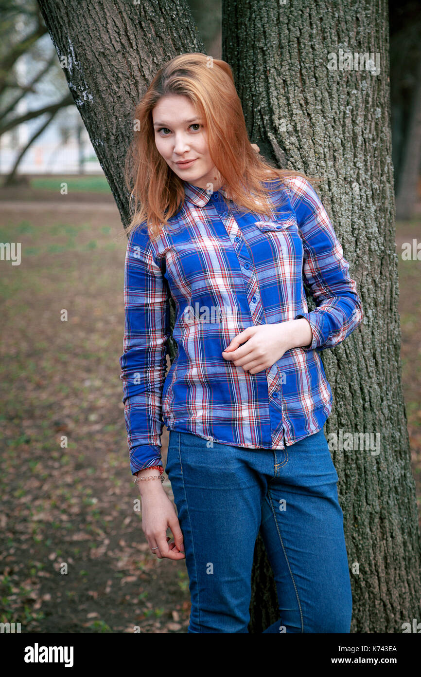 Ritratto di una bella ragazza. Sorridendo, ponendo sulla fotocamera. in una maglietta blu in una gabbia. contro lo sfondo del parco di autunno Foto Stock