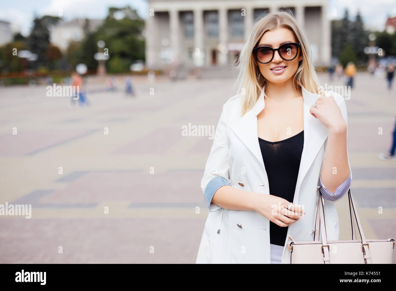 Donna attraente in piedi in un urbano piazza davanti ad un grande edificio storico guardando la telecamera con un caldo sorriso amichevole con copia spazio. Foto Stock