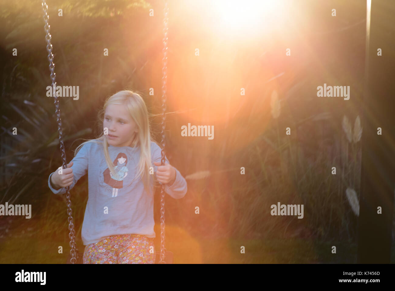 La ragazza oscilla in avanti su un'oscillazione del giardino con il tramonto dietro che viene attraverso gli alberi. REGNO UNITO. 2017 Foto Stock