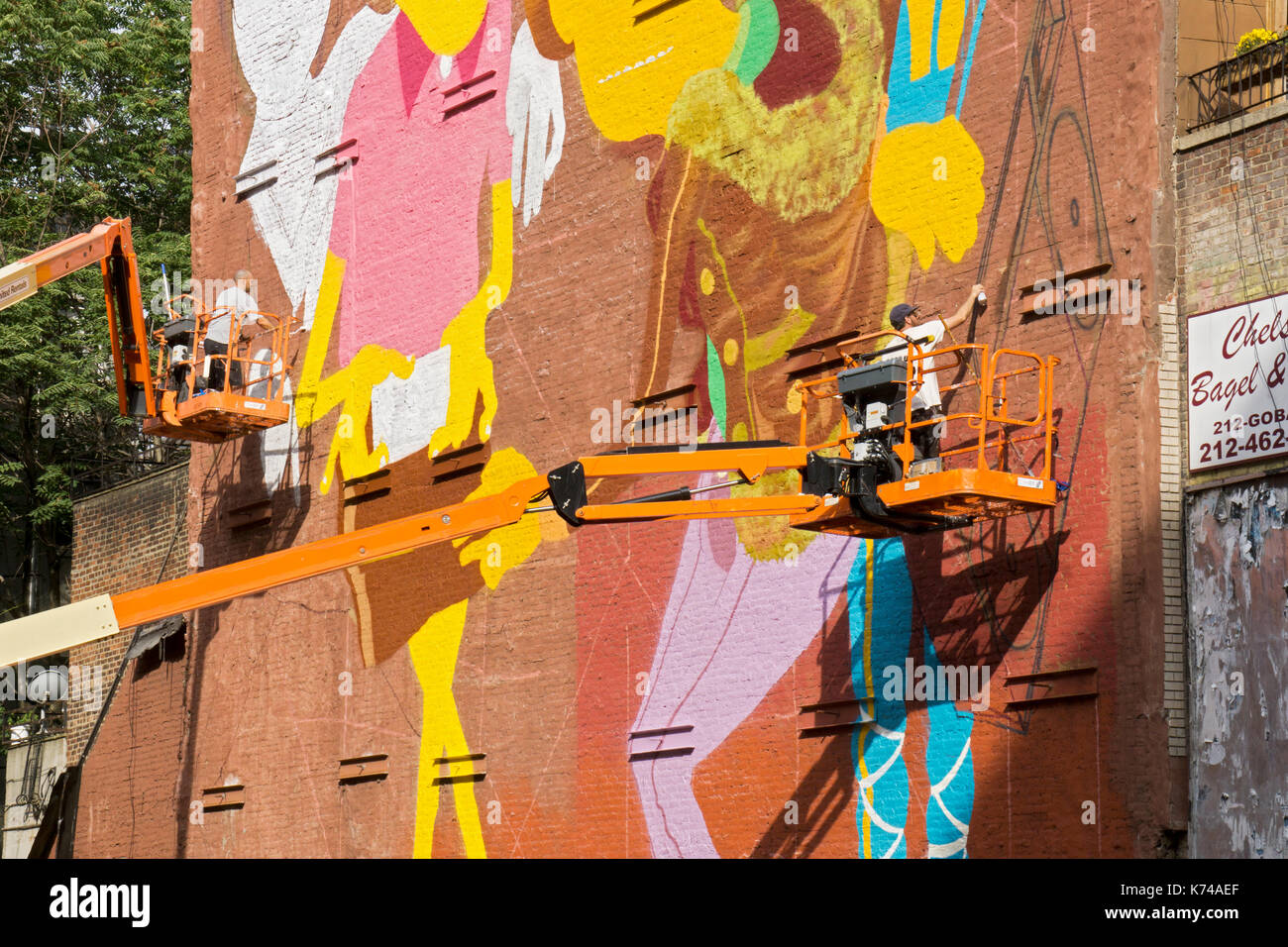 Due muralists su cherry raccoglitori di verniciatura di un enorme parete in un vicoletto sulla West 14th Street off Settima Avenue in Lower Manhattan, New York City. Foto Stock