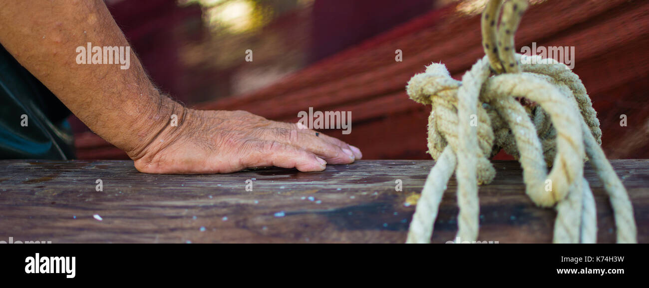 Fisherman's mano con rete da pesca in background. Bagnato e rugosa mano appoggiata su una barca di legno di recinzione. Fisherman's mano accanto alla fune vincolata. Foto Stock