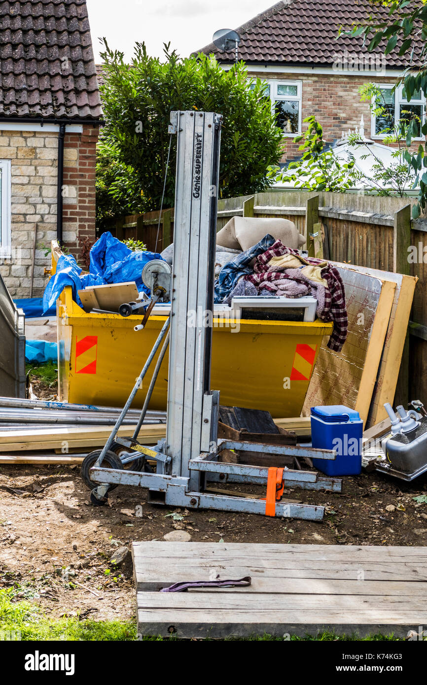 Un grande ingaggiato saltare nel giardino di una casa piena di rifiuti di materiali relativi alla famiglia di un progetto di costruzione. Inghilterra, Regno Unito. Foto Stock