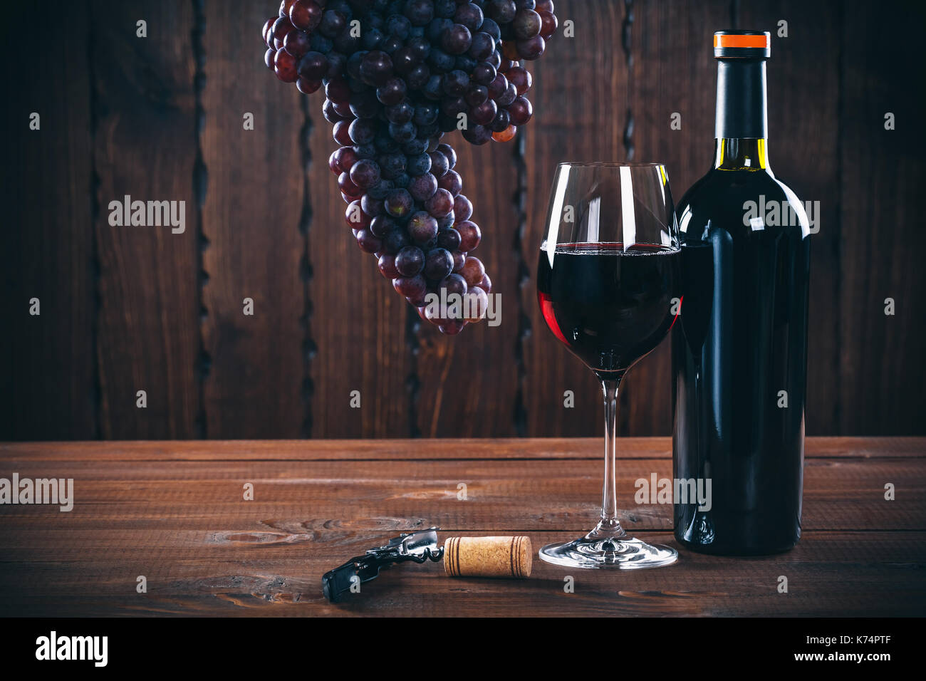 Bottiglia e bicchiere di vino rosso, uva e sughero su sfondo di legno. Foto Stock