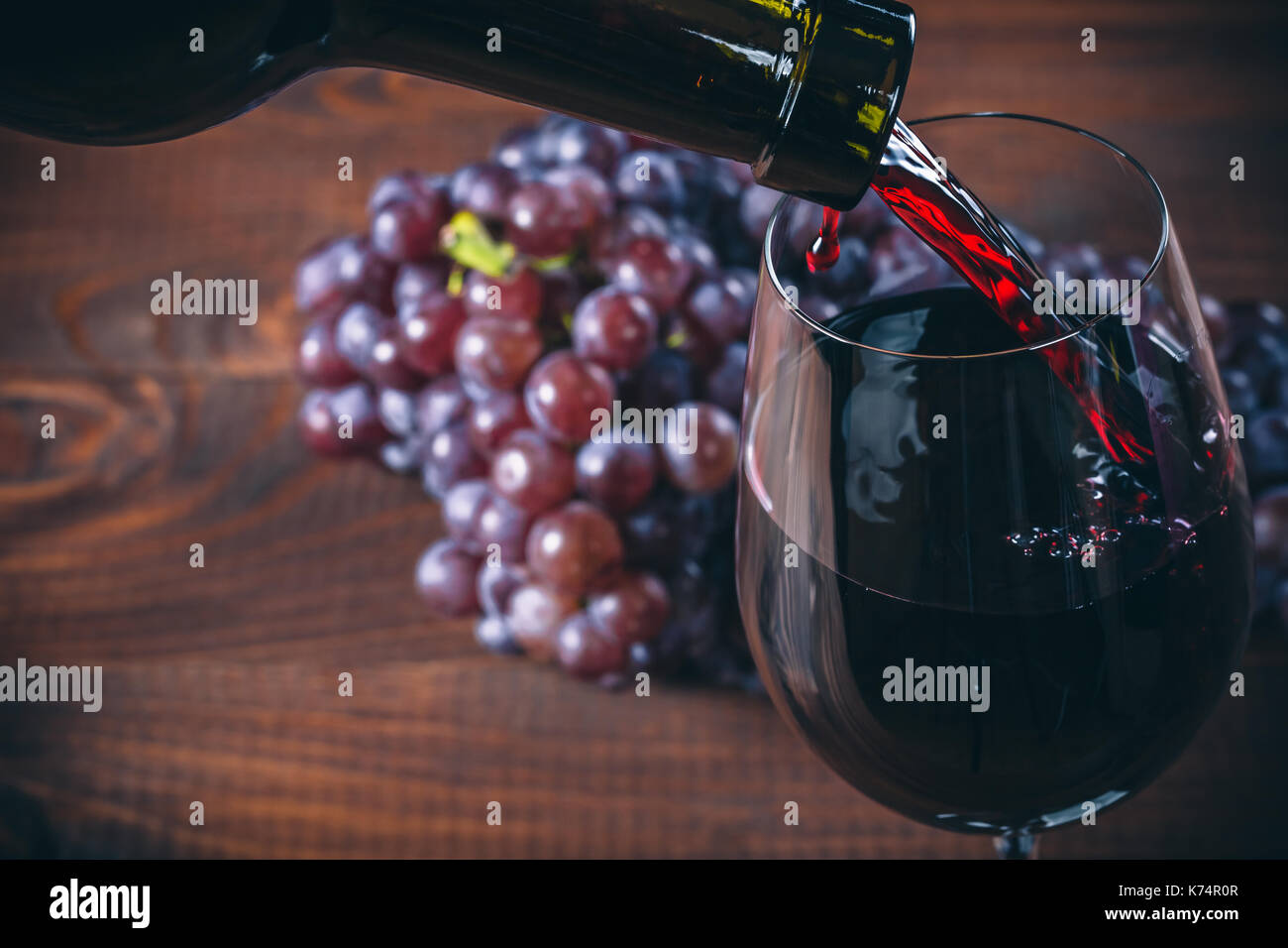 Versare il vino rosso in vetro con un grappolo di uva rossa contro lo sfondo di legno Foto Stock