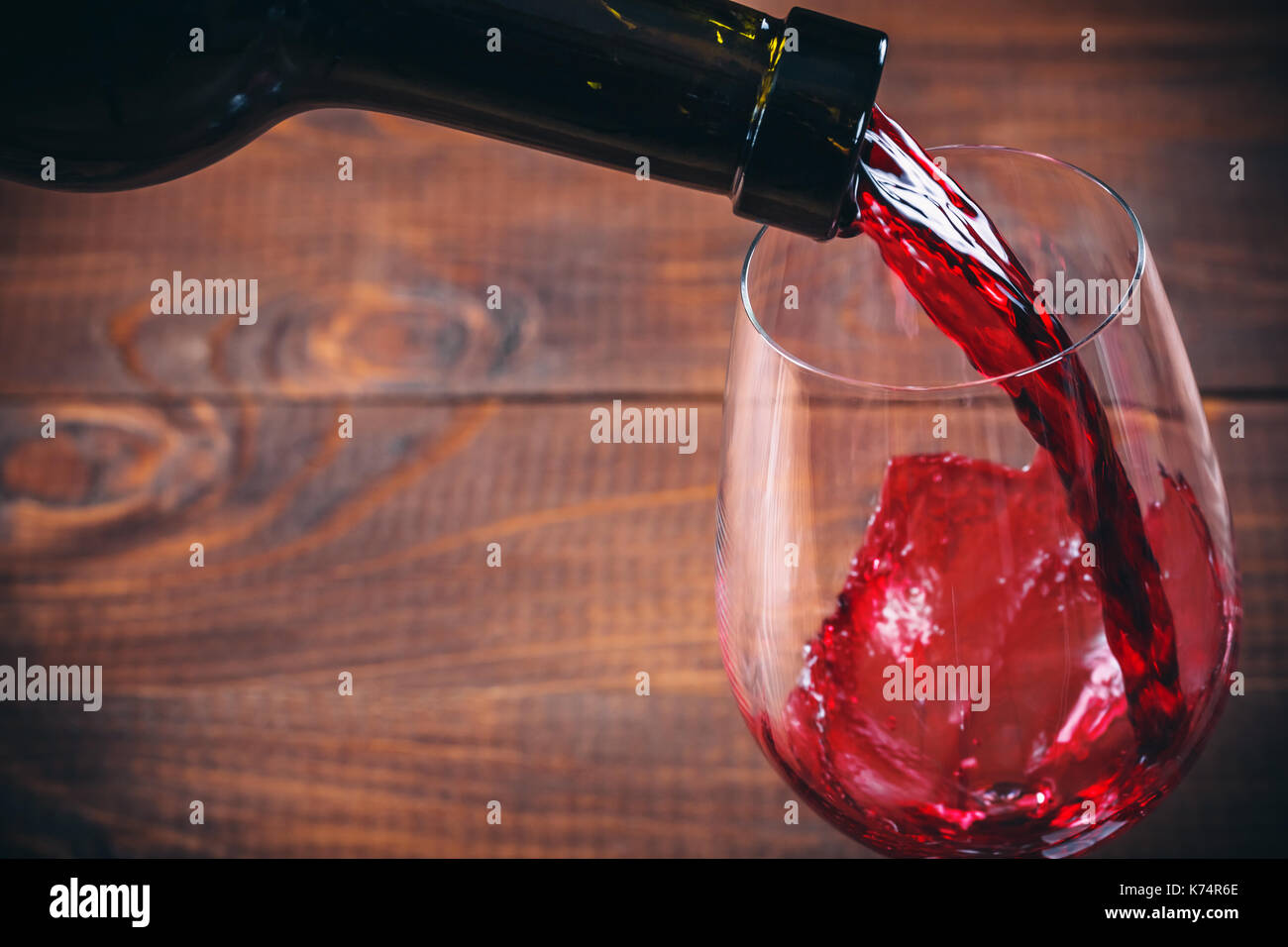 Versare il vino rosso in vetro su sfondo di legno Foto Stock