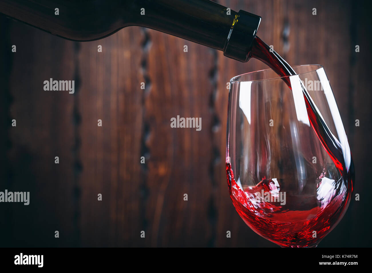 Versare il vino rosso in vetro su sfondo di legno Foto Stock