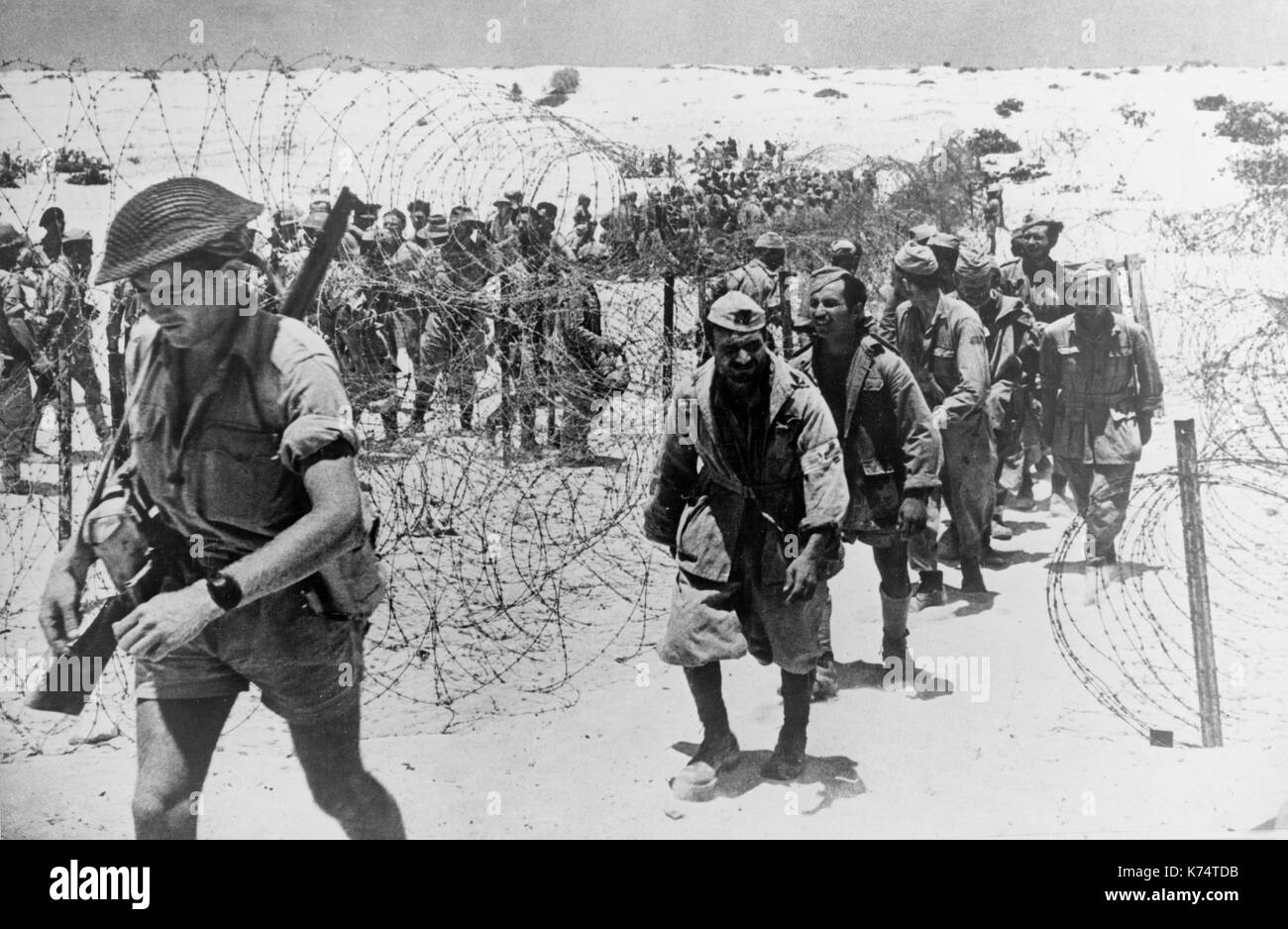 Prigionieri di guerra italiani catturati in combattimenti a El Alamein area inserire un filo spinato enclosure precedute dalla loro protezione, El Alamein, Egitto, 11/1942. Foto Stock