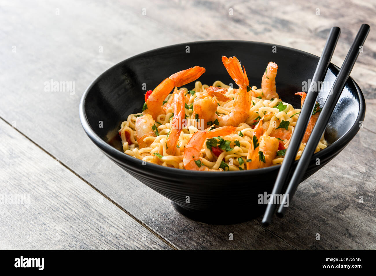 Tagliatelle e gamberetti con verdure in nero ciotola sul tavolo di legno Foto Stock