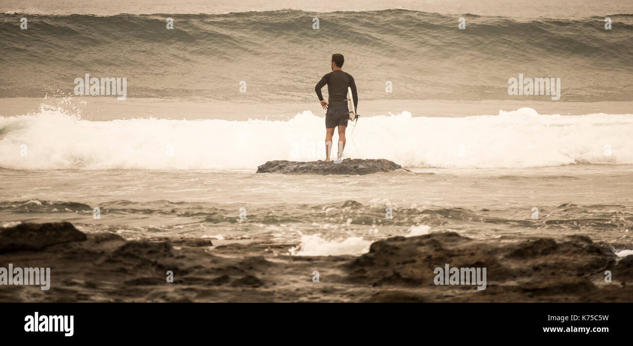 Surfista con la tavola da surf in attesa di un'onda di pausa prima di uscire. Foto Stock