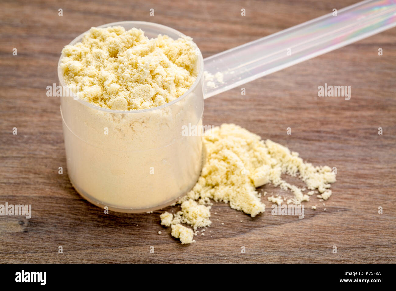 Plastica scoop di misurazione di una proteina di siero di latte in polvere granulare contro uno sfondo di legno Foto Stock