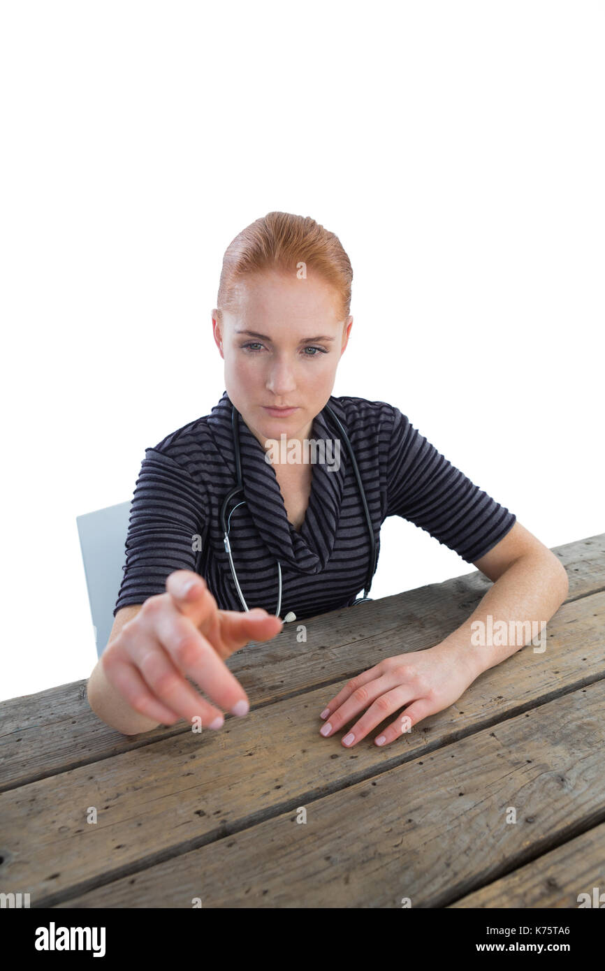 Medico donna toccando interfaccia immaginaria a tavola contro backgroound bianco Foto Stock