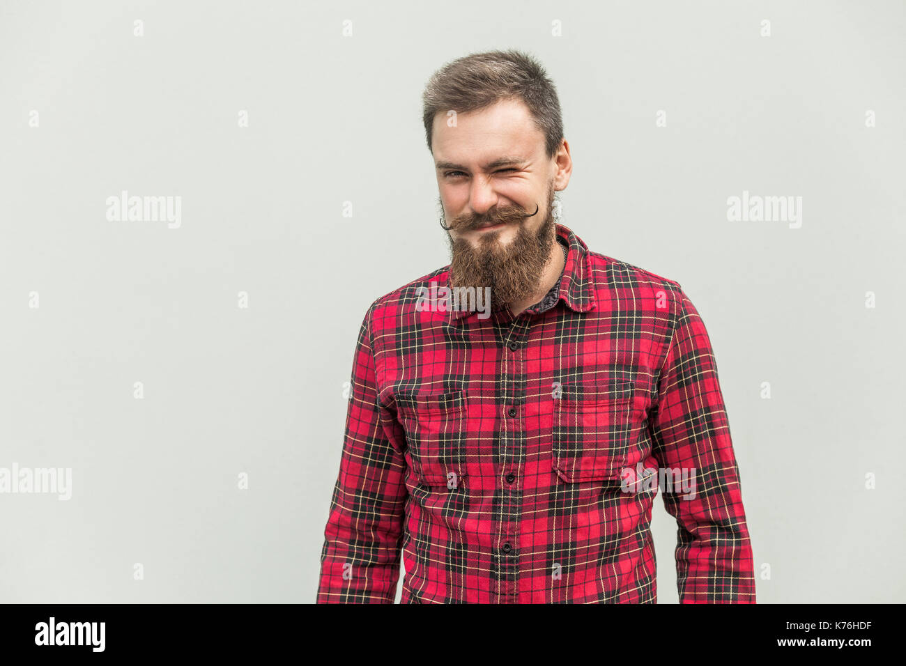 Flirt e wink. spensierata uomo barbuto winked alla fotocamera e sorridente. studio shot, sfondo grigio Foto Stock