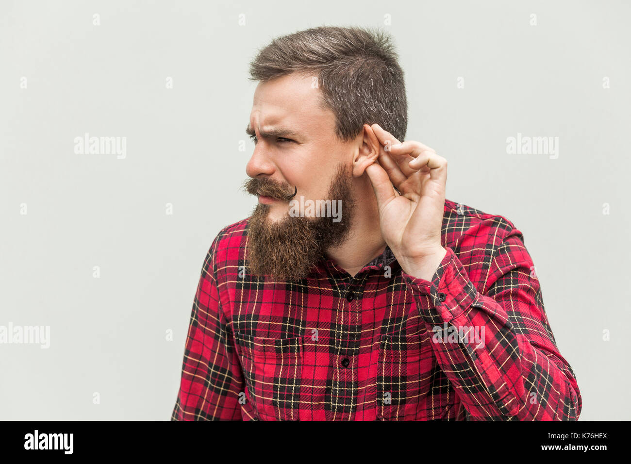 Non riesco a sentire voi. giovane adulto uomo barbuto ascoltare. studio shot, sfondo grigio Foto Stock