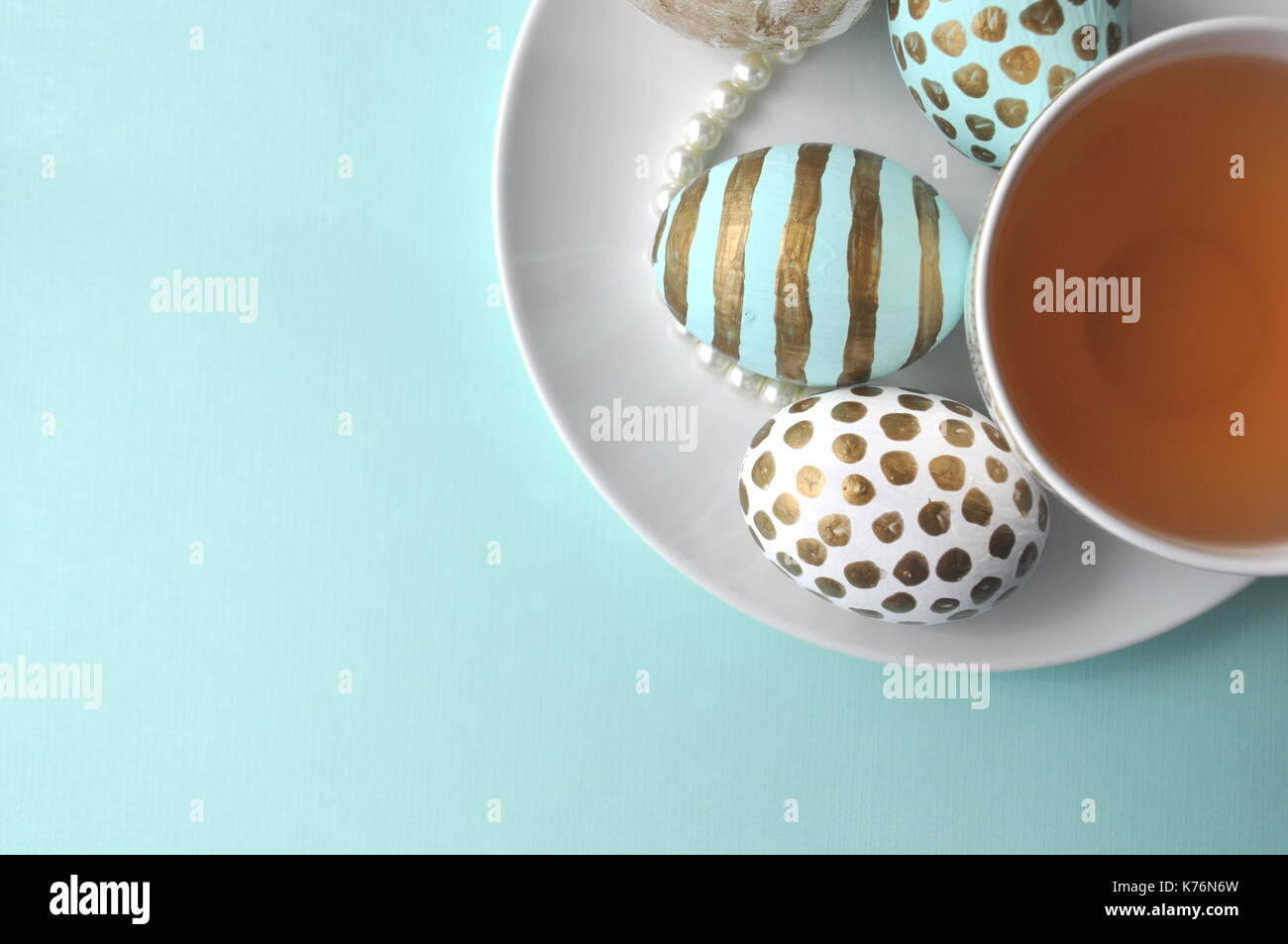 Decorate le uova di pasqua con motivi floreali notebook e la tazza di tè alla menta su aqua teal blu sfondo turchese con spazio di copia Foto Stock
