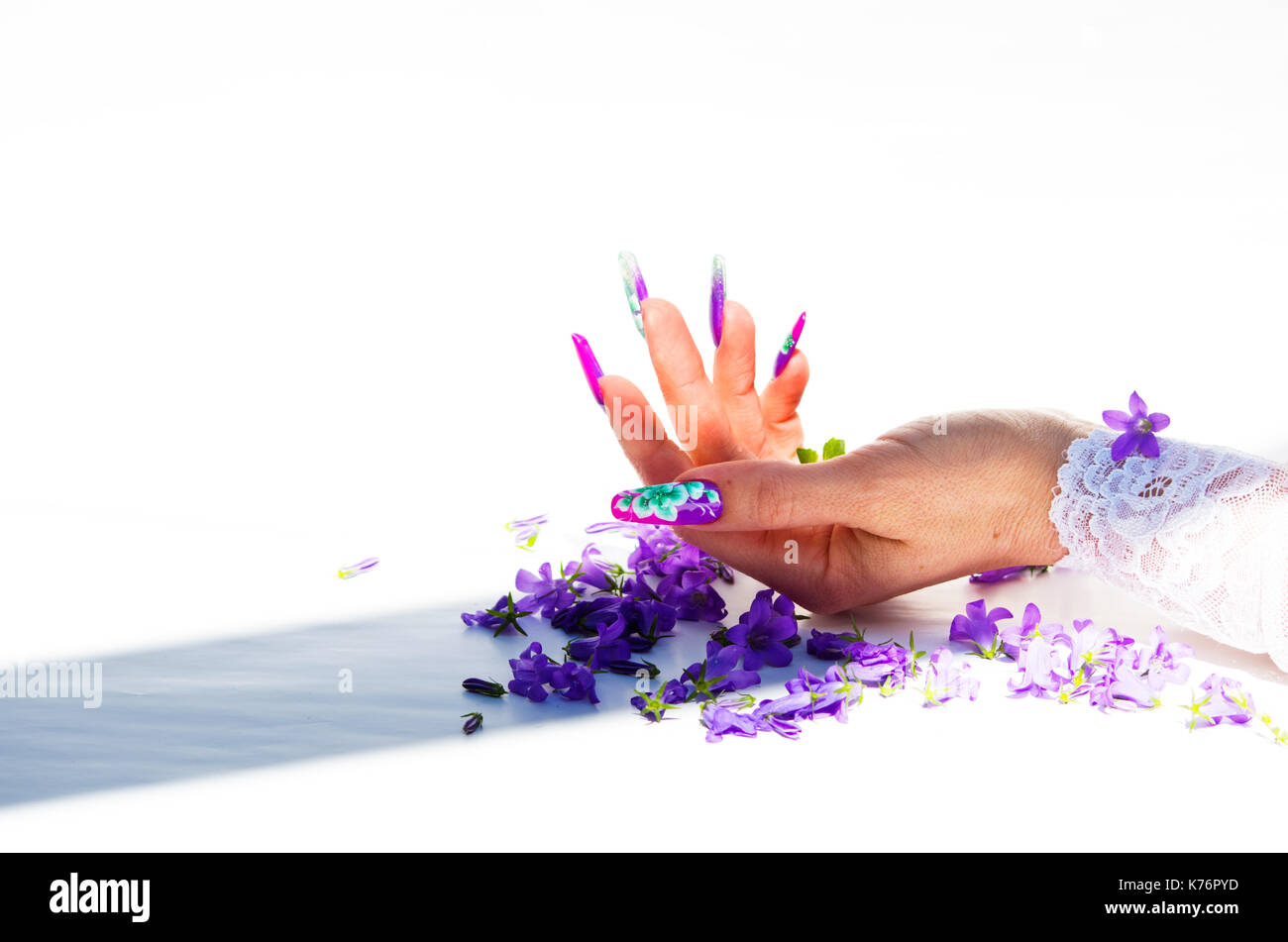 Mano con chiodi ricostruito e decorato con fiori colorati e portare blu e floreale bianco su sfondo bianco, bella novità per la primavera e l'estate Foto Stock