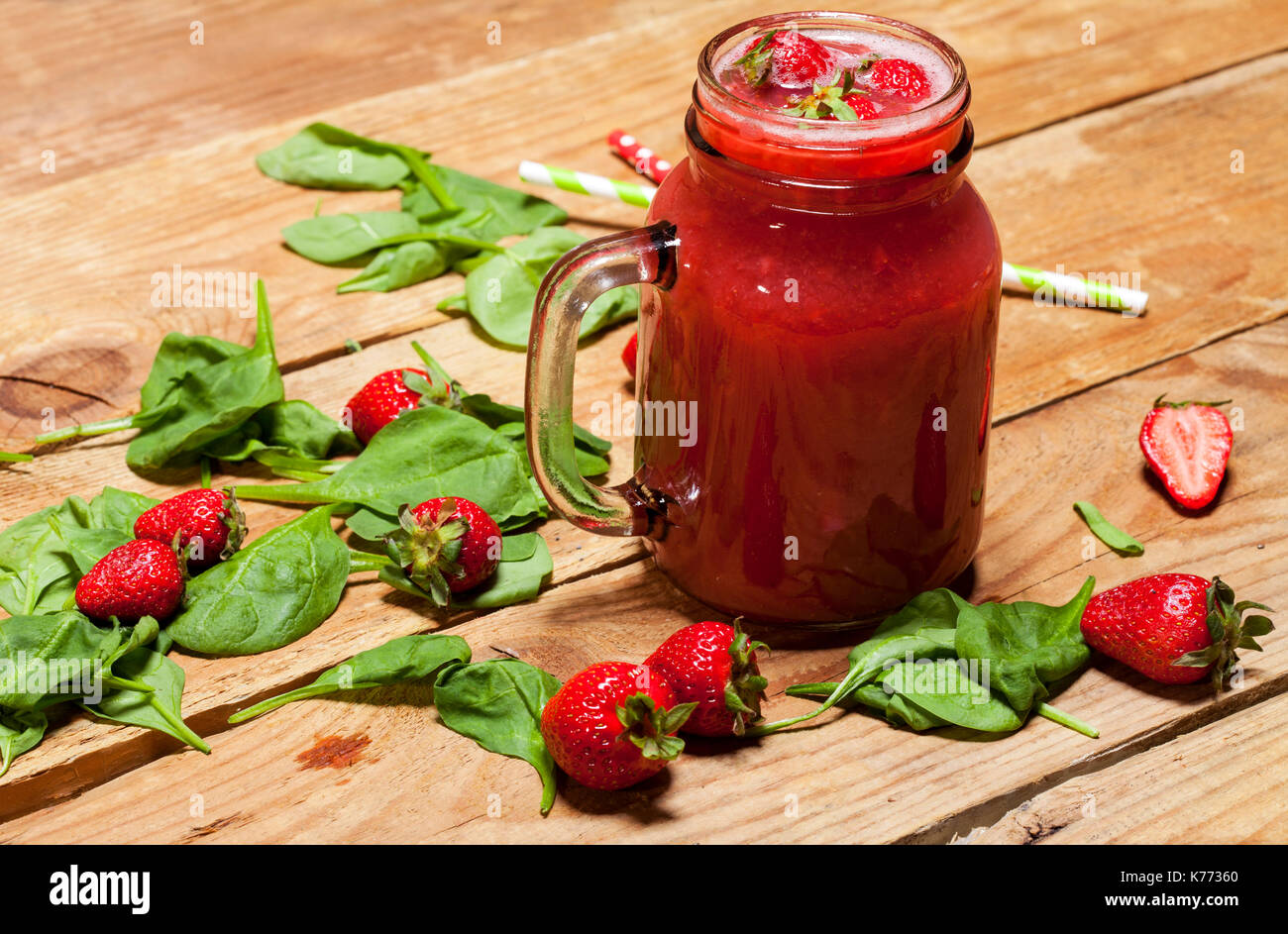 Frullato di fragole o frullato in un vaso e foglie di spinaci su sfondo di legno, cibo sano per la prima colazione e snack Foto Stock