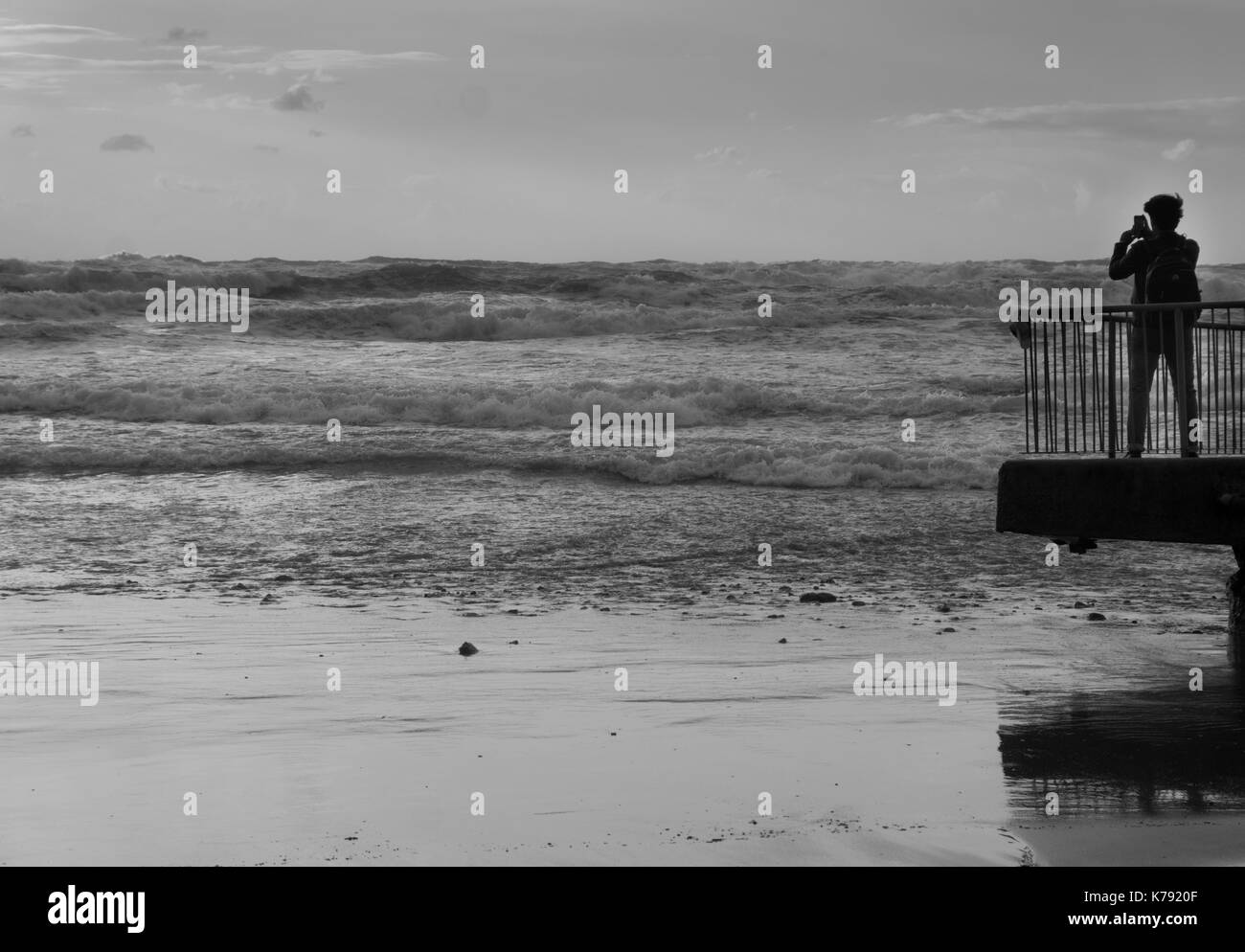 Vista posteriore di una turistica prendendo foto della tempesta di mare con lo smartphone nella parte anteriore di mare in bianco e nero Foto Stock
