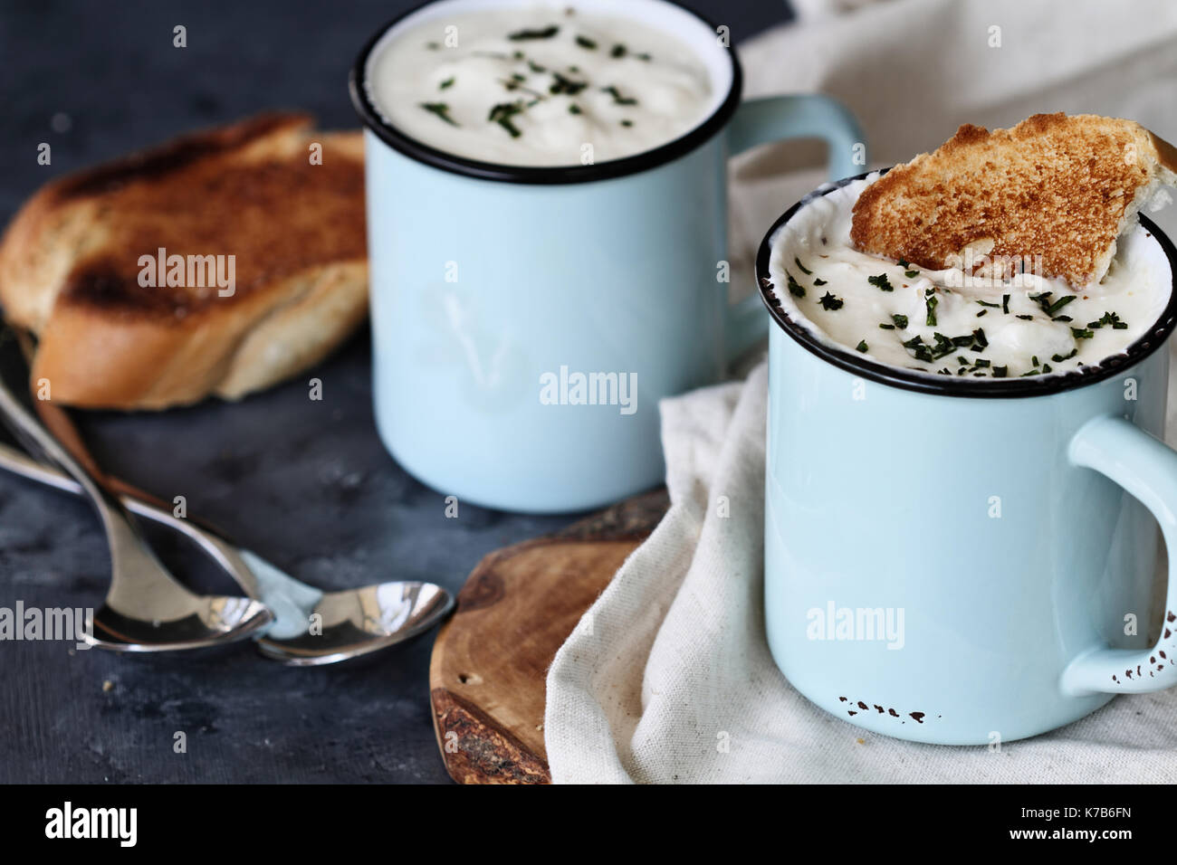 Calda zuppa di patate con erba cipollina essiccata e fette di pane tostato in smalto rustico tazze. estrema profondità di campo con il fuoco selettivo sulla tazza in foreg Foto Stock