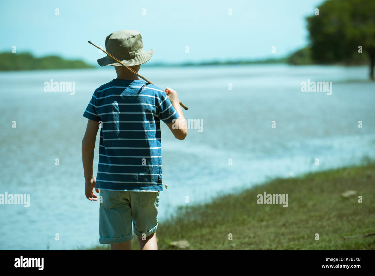 Ragazzo camminando lungo la riva del lago con la canna da pesca, vista posteriore Foto Stock