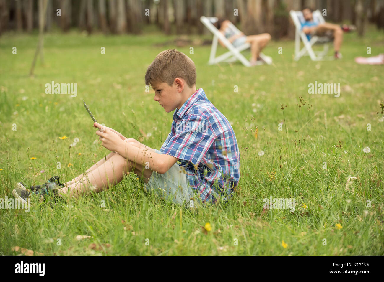 Ragazzo seduto su un prato guardando a tavoletta digitale Foto Stock